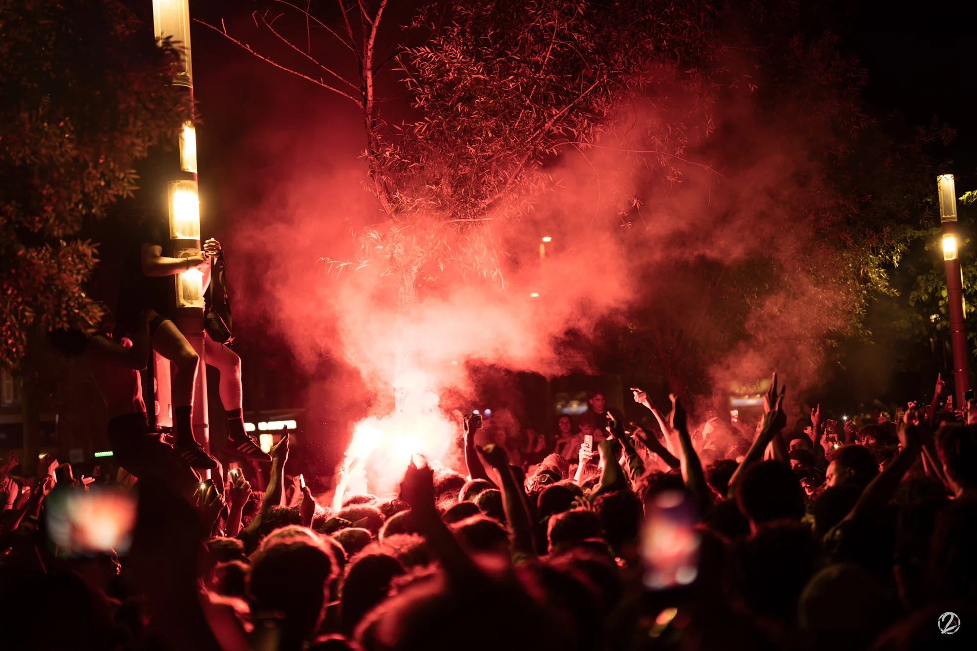 Foule nocturne éclairée par un fumigène rouge.