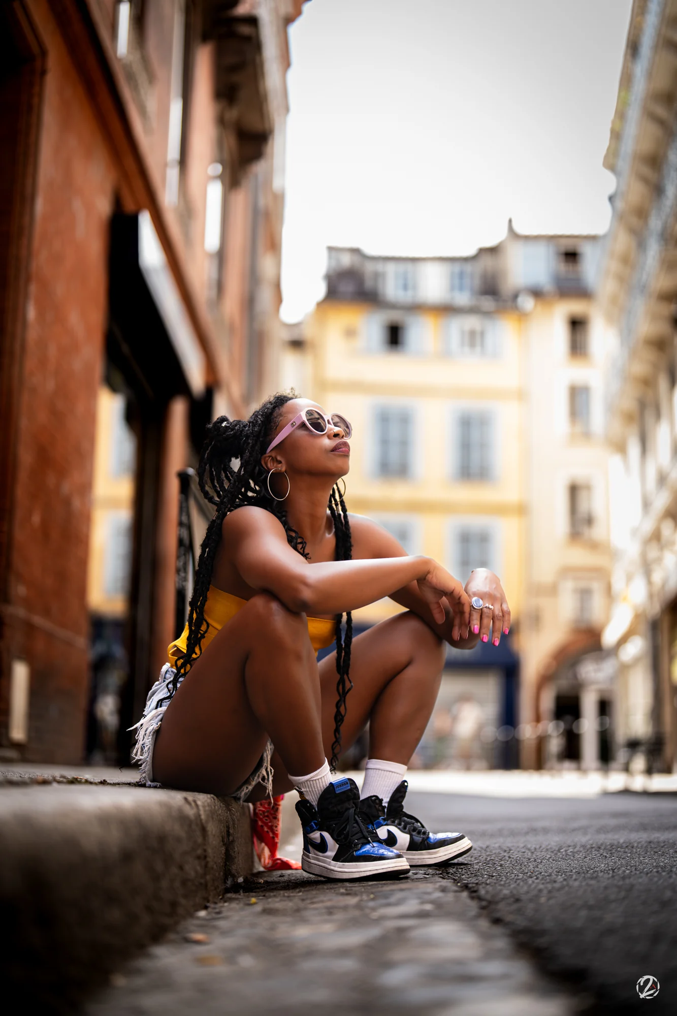 Portrait assis dans une ruelle, lunettes roses et haut jaune.