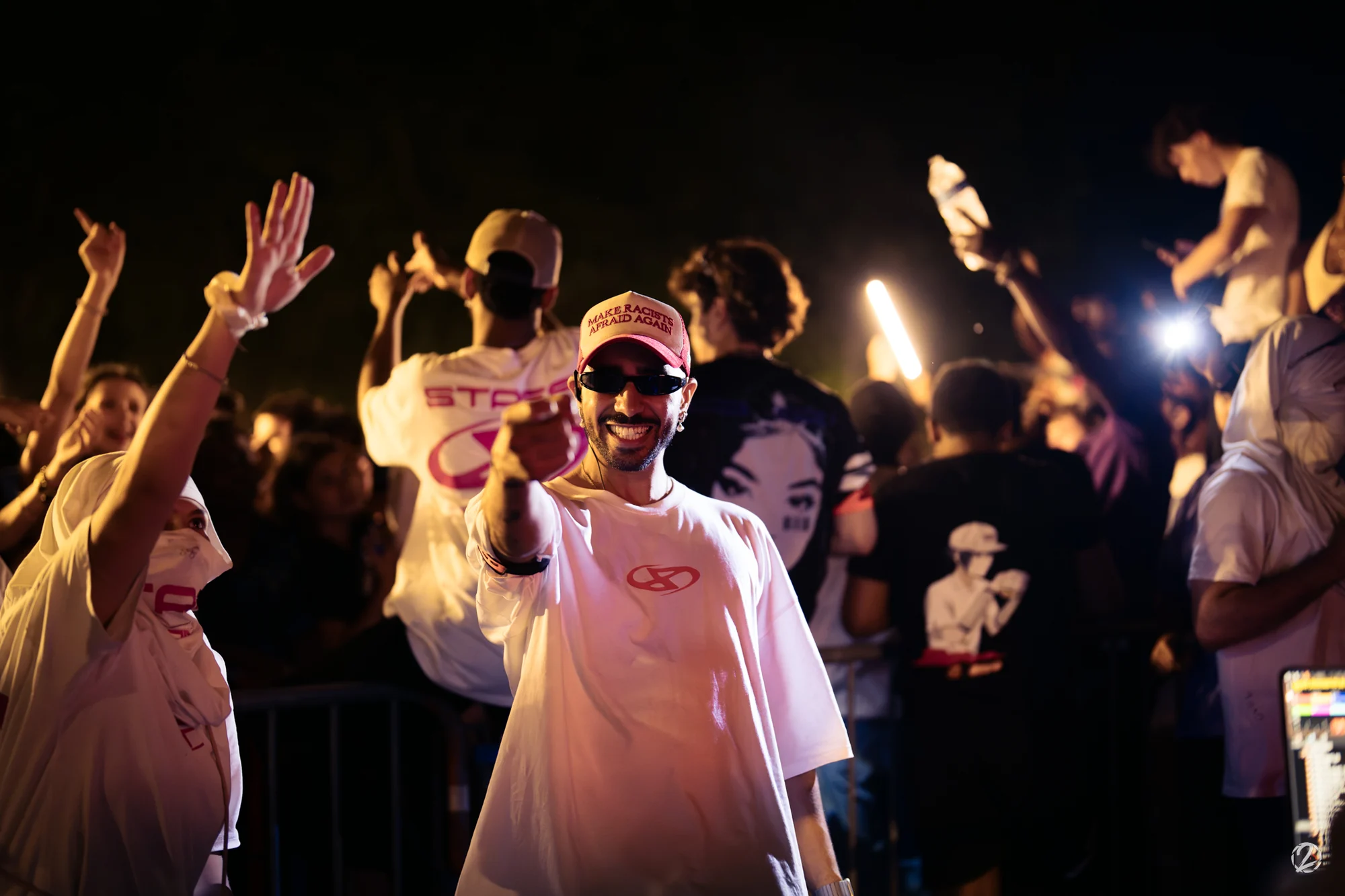 Un participant souriant en casquette rose au milieu d’une foule de nuit.