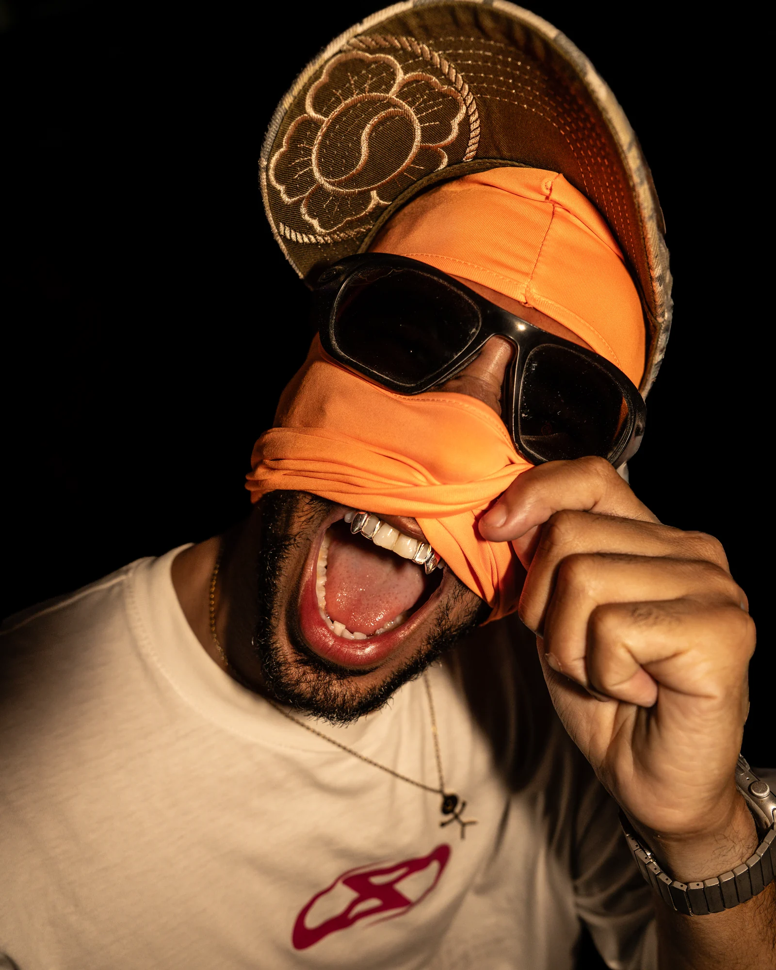 Gros plan expressif, cagoule orange, casquette et lunettes.